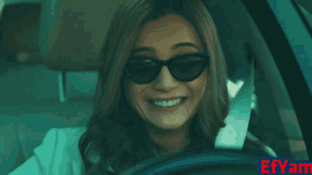 a woman wearing sunglasses laughs while driving a car with a smiley face behind her
