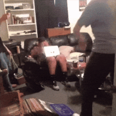 a person sitting on a couch with a laptop on their lap while a man stands in front of them