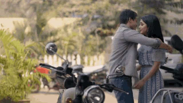 a man and a woman are hugging in front of a motorcycle parked on the side of the road .