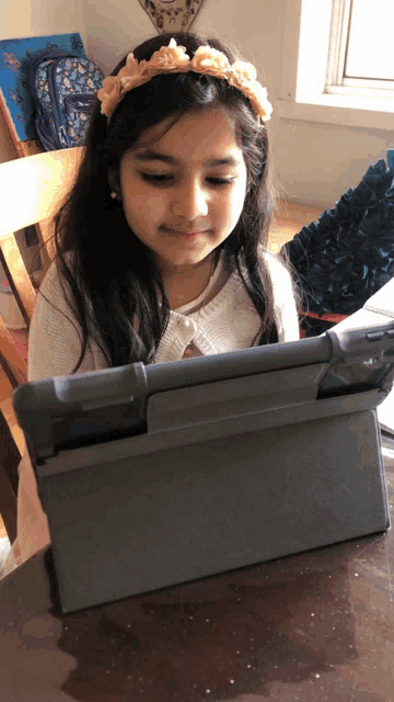 a young girl wearing a flower headband is looking at a tablet