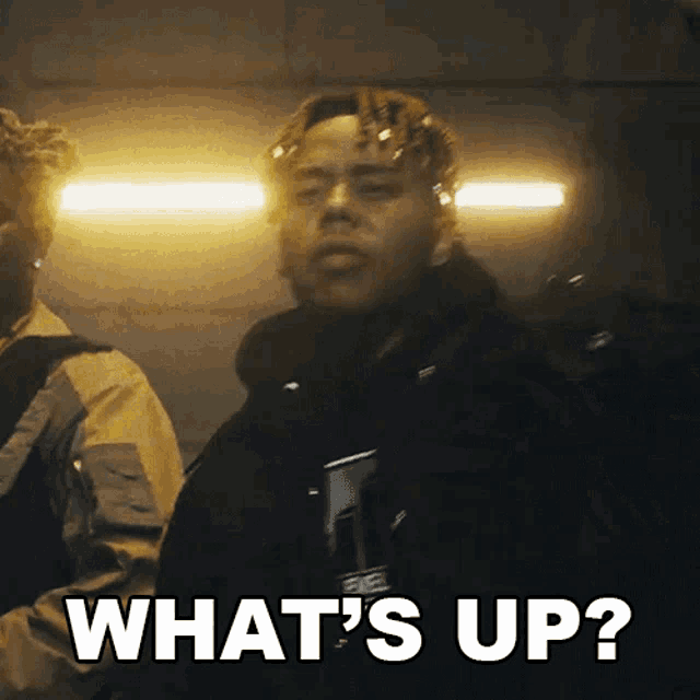 a man in a black jacket says " what 's up " while standing next to another man