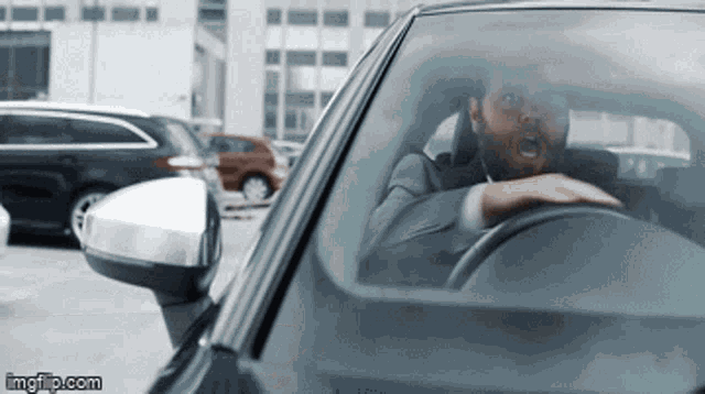 a man in a suit and tie is driving a car with his mouth open