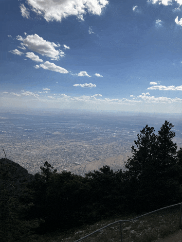 a view of a city from a mountain with a blue sky and clouds