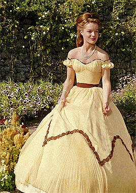 a woman in a yellow dress is standing in front of a stone wall