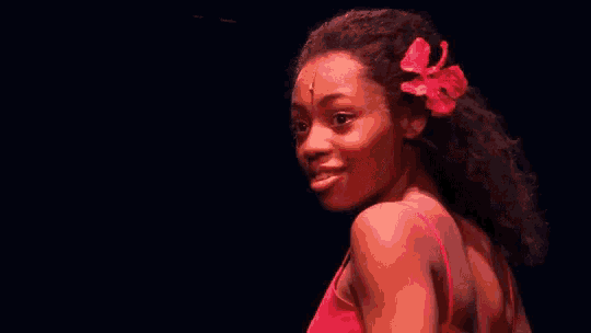a woman in a red dress with a red flower in her hair is smiling on a stage .