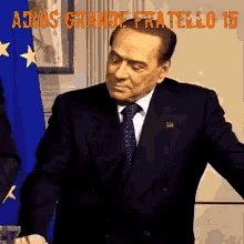 a man in a suit and tie stands in front of a blue and white flag with the words adios grande fratello 15 above him