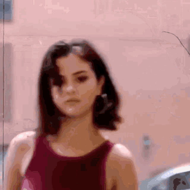 a woman in a red tank top stands in front of a pink wall .