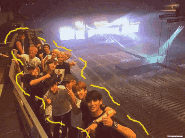 a group of young men are posing for a picture in front of a stage with a purple light coming from the top