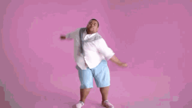 a fat man in a white shirt and blue shorts is dancing on a pink background .
