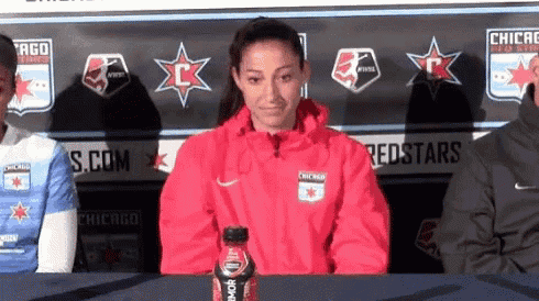 a woman in a chicago redstars jacket sits at a table with a gatorade bottle