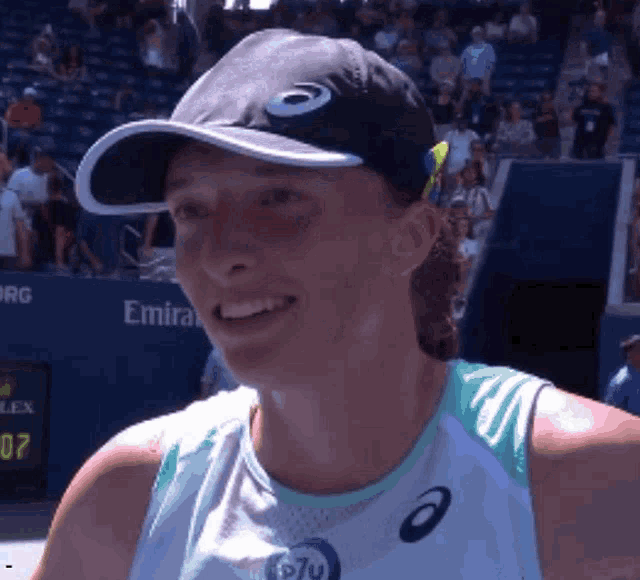 a woman wearing an asics hat is smiling in front of a emirates banner