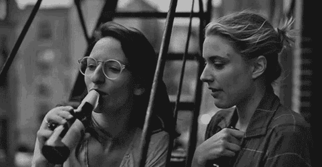 two women are standing next to each other on a fire escape talking to each other in a black and white photo .