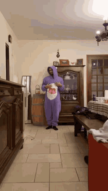 a man in a purple care bear onesie is holding a care bear
