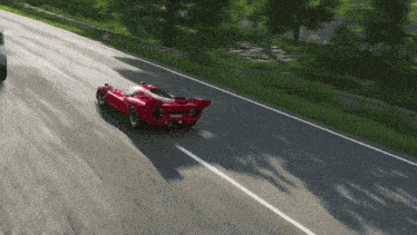 a red sports car is driving down a road with trees in the background