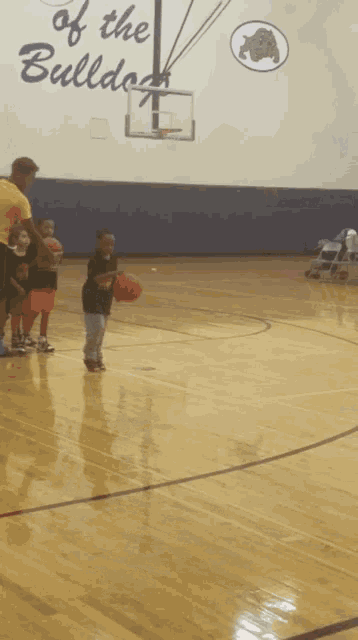 a group of kids are playing basketball in front of a wall that says " of the bulldog "