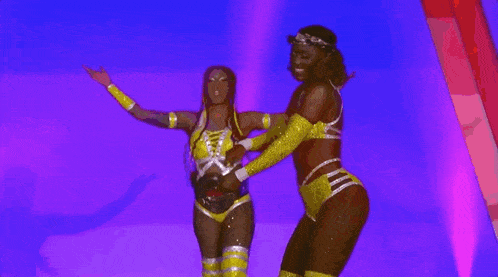 two women in yellow and black wrestling outfits are dancing on a stage