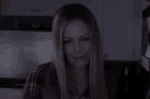 a woman in a plaid shirt is looking at the camera in a dark room .