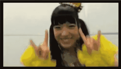 a girl wearing a yellow jacket is making a peace sign with her hands