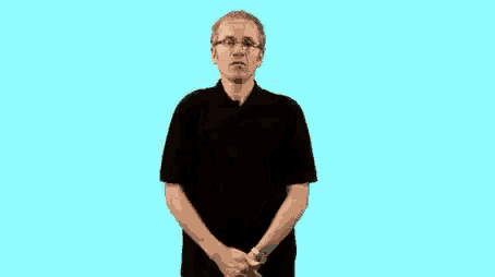 a man wearing glasses and a black shirt is making a funny face while standing in front of a blue background .