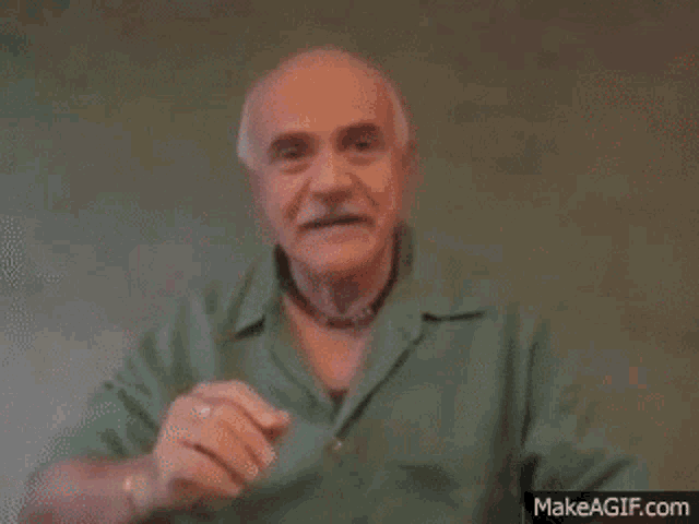 an older man in a green shirt is making a gesture with his hand