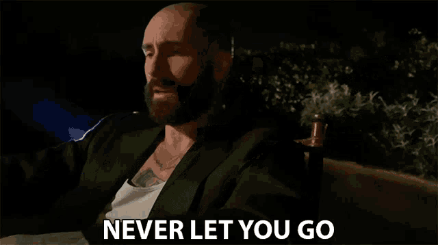 a man with a beard is sitting in a chair and says " never let you go "