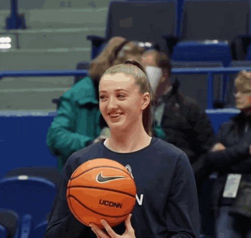a woman in a uconn shirt holds a basketball