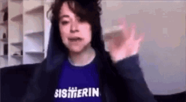 a woman wearing a purple shirt and a black hoodie is waving .