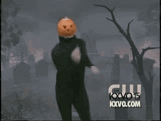 a man with a pumpkin on his head is running in front of a cemetery