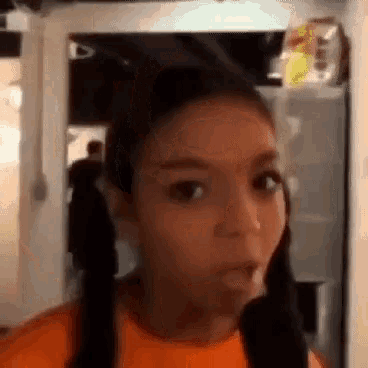 a girl with pigtails is making a funny face while wearing an orange shirt .