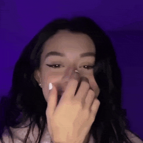 a woman is covering her mouth with her hand in front of a purple wall .