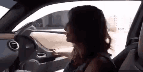 a woman is sitting in the driver 's seat of a car and looking out the window .