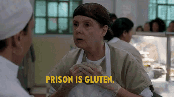 a woman in an apron is talking to another woman in a kitchen and the words prison is gluten are above her .