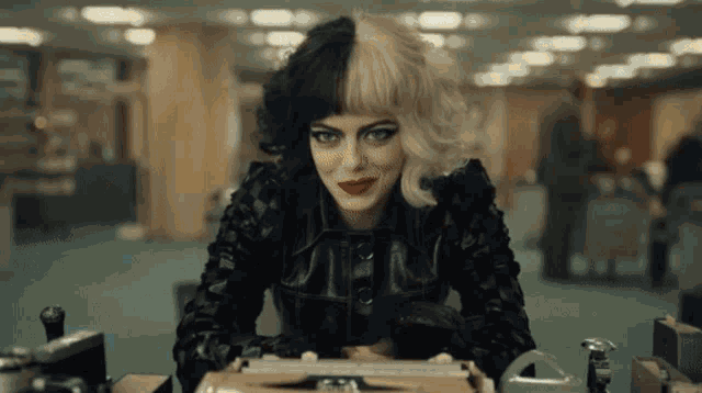 a woman with half black and half white hair sits at a desk with a typewriter