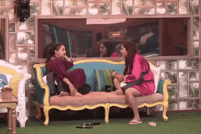 two women are sitting on a couch in front of a mirror talking to each other