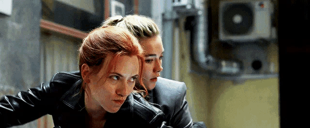 two women in leather jackets are standing next to each other in a dark room .