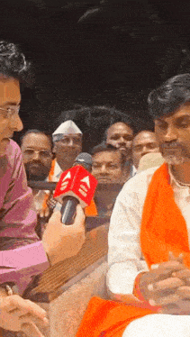 a man is being interviewed by a reporter with a microphone that says ' aaj ' on it