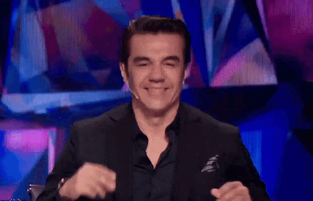 a man in a black suit is smiling in front of a blue background