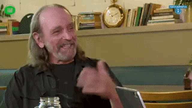 a man with long hair and a beard is sitting at a table in front of a bookshelf .
