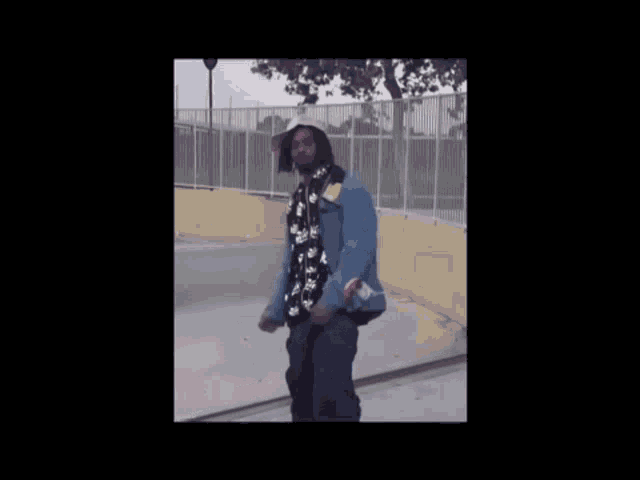 a man wearing a hat and a denim jacket is standing on a skate park