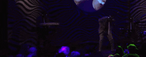a man playing a keyboard in front of a purple and white striped wall