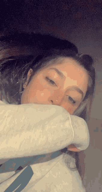 a woman covering her mouth with her sleeve while wearing a white sweatshirt