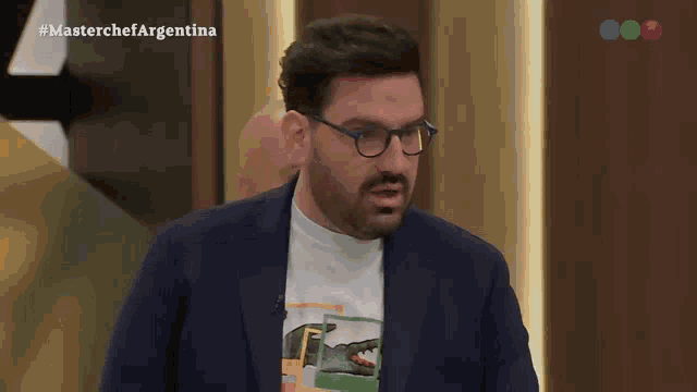 a man wearing glasses and a t-shirt with a crocodile on it is on a tv show called masterchef argentina