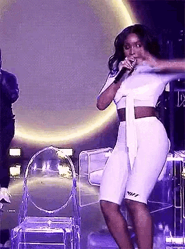 a woman in a white outfit is singing into a microphone while dancing on stage .