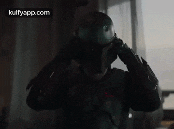 boba fett is wearing a helmet and standing in front of a window in a room .