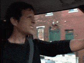 a man in a black shirt is driving a car with his arm out