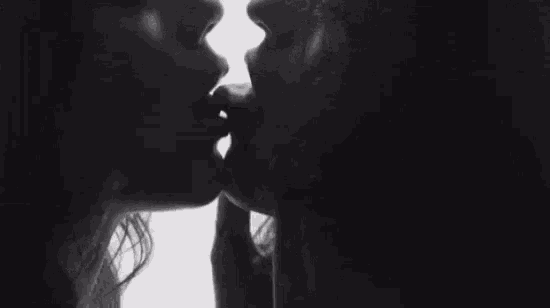 it is a black and white photo of a man and woman kissing .