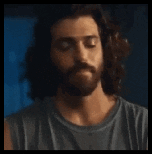 a man with long hair and a beard is holding a wooden stick in his hand .