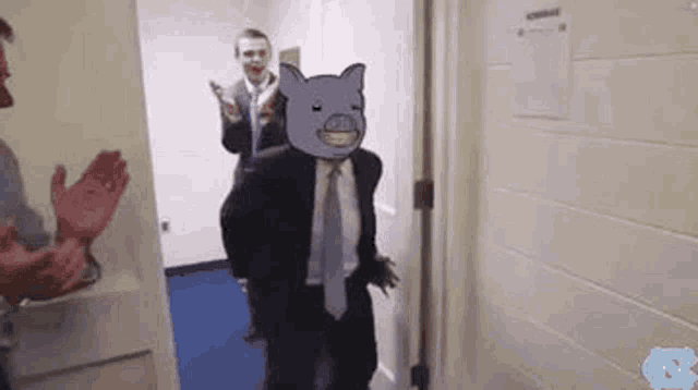 a man in a suit and tie is standing in a hallway with a cartoon pig on his face .