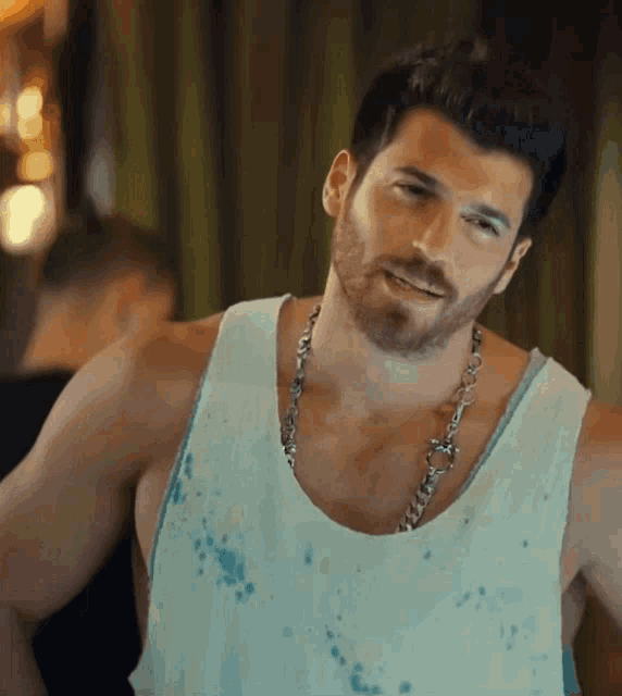 a man with a beard wears a tank top and a necklace