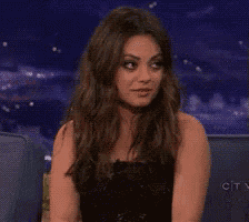 a woman in a black dress is sitting in a chair making a funny face .